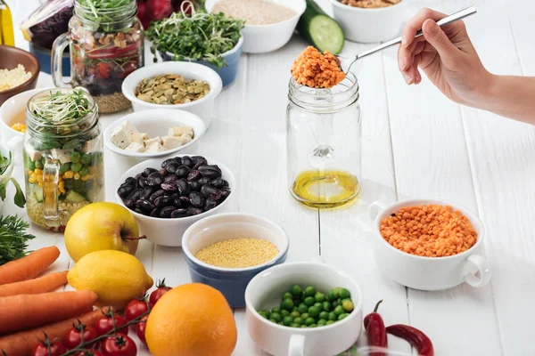 Cropped view of woman adding couscous in glass jar with oil on wooden white table — Stock Photo