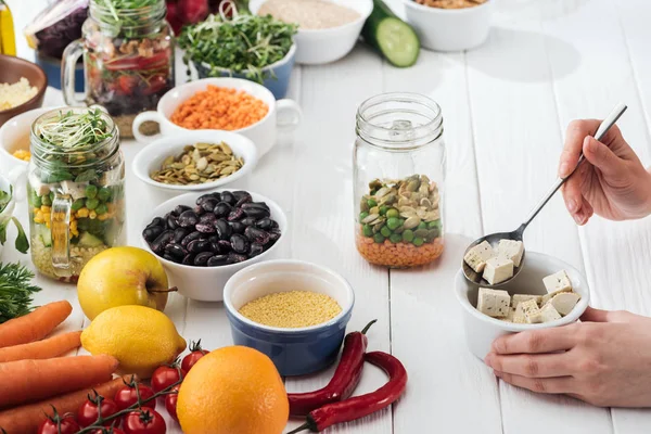 Cropped view of woman adding tofu cheese in glass jar on wooden white table — Stock Photo