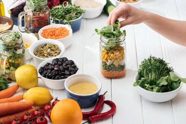 Cropped view of woman cooking salad in glass gar on wooden white table — Stock Photo