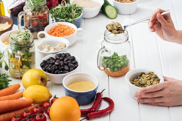 Cropped view of woman adding pumpkin seeds in glass jar on wooden white table — Stock Photo