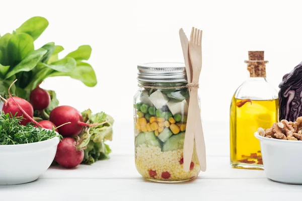 Fresh vegetable salad in glass jar near oil and radish isolated on white — Stock Photo