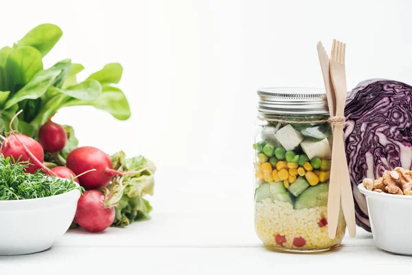 Ensalada de verduras frescas en frasco de vidrio cerca de rábano, col roja y frutos secos aislados en blanco - foto de stock