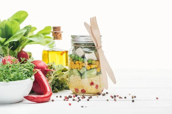 Salada de legumes frescos em jarra de vidro com talheres de madeira isolados em branco — Fotografia de Stock