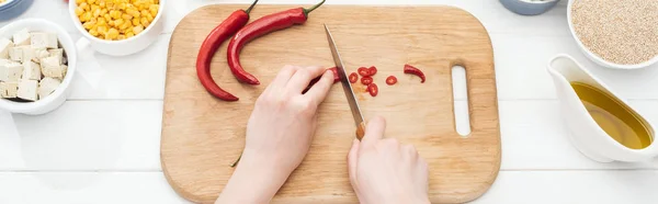 Abgeschnittene Ansicht einer Frau, die Chilischoten auf einem hölzernen Schneidebrett auf weißem Tisch schneidet, Panoramaaufnahme — Stockfoto