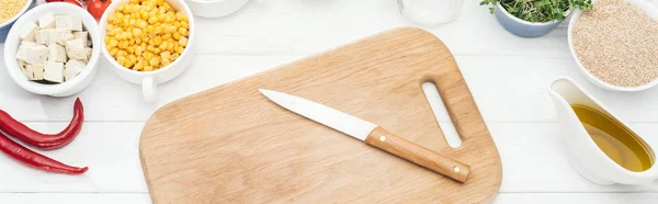 Top view of wooden chopping board with knife on white table, panoramic shot — Stock Photo