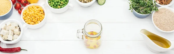 Vista superior del frasco de vidrio con aceite y chile cerca de frutas y verduras cerca de frascos de vidrio en la mesa blanca de madera, plano panorámico - foto de stock