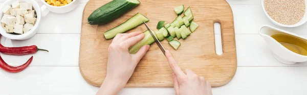 Vue recadrée d'une femme coupant du concombre sur une table blanche en bois, vue panoramique — Photo de stock