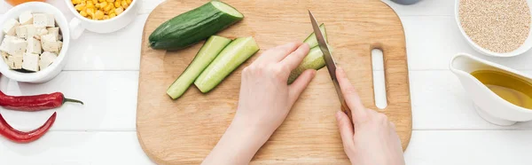 Partial view of woman chopping cucumber on wooden white table, panoramic shot — Stock Photo