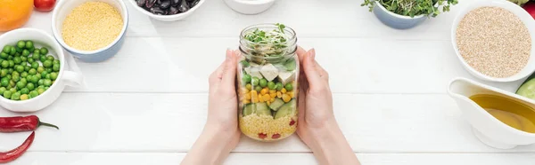 Vista cortada da mulher segurando frasco de vidro com salada fresca na mesa branca de madeira, tiro panorâmico — Fotografia de Stock