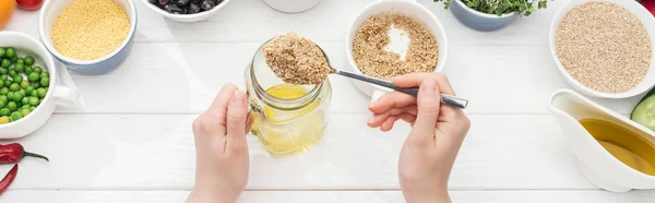 Cropped view of woman adding couscous in jar with oil on wooden white table, panoramic shot — Stock Photo