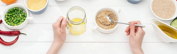 Partial view of woman adding couscous in jar with oil on wooden white table, panoramic shot — Stock Photo