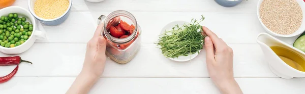 Cropped view of woman holding jar with salad and green sprouts on wooden white table , panoramic shot — Stock Photo