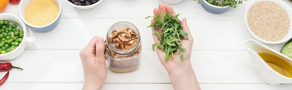 Vue recadrée de femme ajoutant des germes dans un bocal avec des noix sur une table blanche en bois, vue panoramique — Photo de stock