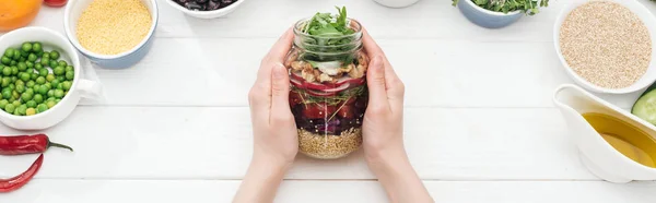 Vista ritagliata della donna che tiene il vaso con gustosa insalata sul tavolo bianco in legno, colpo panoramico — Foto stock