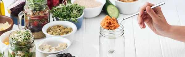 Cropped view of woman adding couscous in glass jar on wooden white table, panoramic shot — Stock Photo