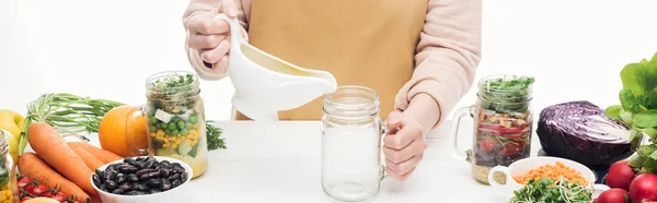 Vista ritagliata della donna in grembiule aggiungendo verdi al vaso di vetro con fagioli su tavolo di legno isolato su bianco, colpo panoramico — Foto stock