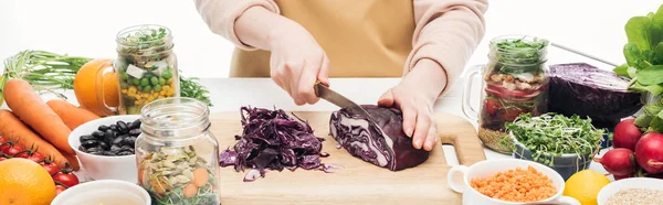 Cropped view of woman in apron cutting red cabbage on wooden table isolated on white, panoramic shot — Stock Photo