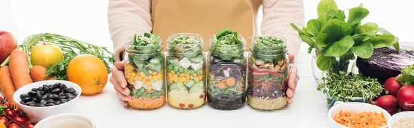 Vue recadrée de la femme avec bocaux en verre avec salade sur table en bois isolé sur blanc, vue panoramique — Photo de stock