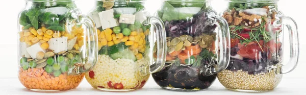 Delicious vegetable salad in glass jars with handles on wooden white table isolated on white, panoramic shot — Stock Photo