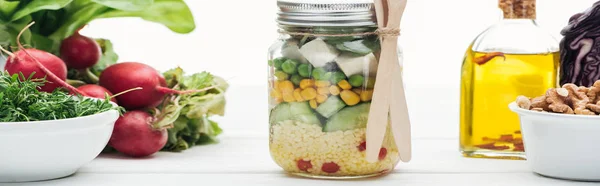 Panoramic shot of fresh vegetable salad in glass jar near oil and radish isolated on white — Stock Photo