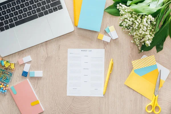 Vista superior de la lista semanal, papelería y computadora portátil en la mesa de madera - foto de stock