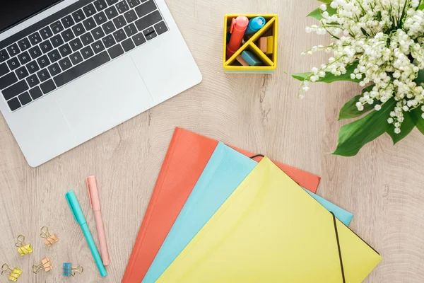 Ansicht von Ordnern, Schreibwaren, Laptop und Blumen auf Holztisch — Stockfoto