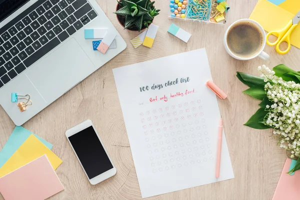 Vista superior da lista de verificação de 100 dias, artigos de papelaria e laptop com smartphone na mesa de madeira — Fotografia de Stock