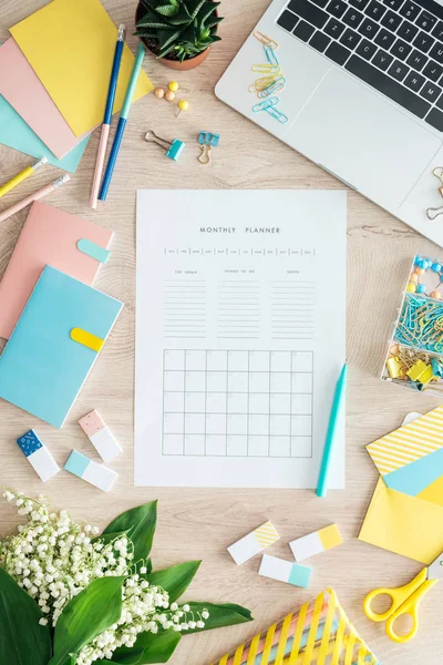 Vista superior do planejador mensal, artigos de papelaria, flores e laptop na mesa de madeira — Fotografia de Stock