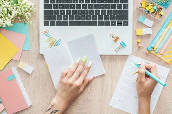 Ausgeschnittene Ansicht einer Frau, die hinter einem Holztisch mit Laptop, Schreibwaren und Wochenliste sitzt — Stockfoto