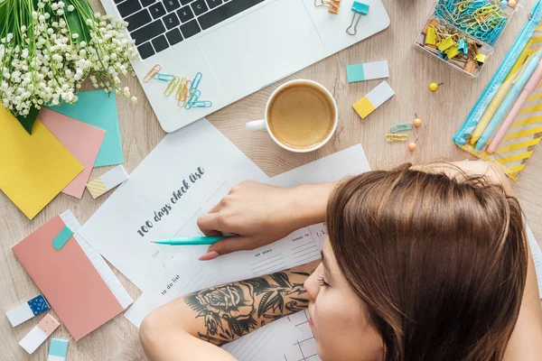 Top view of woman sleeping behind wooden table with stationery, laptop and planners — Stock Photo