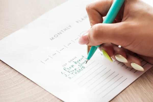 Vista recortada de la mujer escribiendo notas sobre planificador mensual, la celebración de la pluma verde en la mano - foto de stock