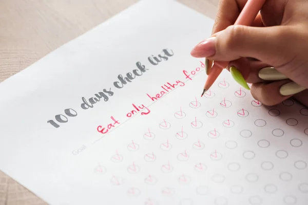 Ausgeschnittene Ansicht einer Frau, die Notizen auf 100 Tage Checkliste schreibt, mit grünem Stift in der Hand — Stockfoto