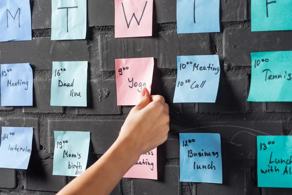 Cropped view of woman attach pink sticker note on black brick wall — Stock Photo