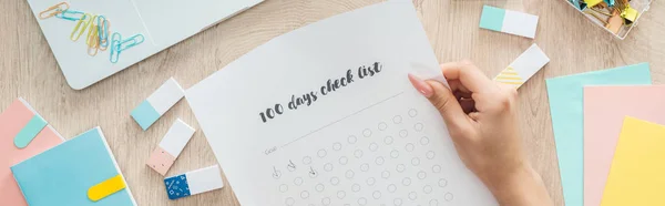 Cropped view of woman holding 100 days challenge list in hands over wooden table with stationery — Stock Photo