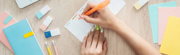 Vista recortada de la mujer escribiendo notas en la lista de hacer, sentado detrás de la mesa de madera con artículos de papelería - foto de stock