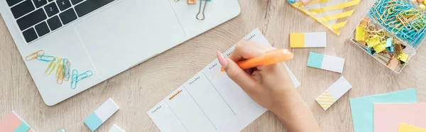 Vista recortada de la mujer escribiendo notas en la lista de hacer, sentado detrás de la mesa de madera con artículos de papelería - foto de stock