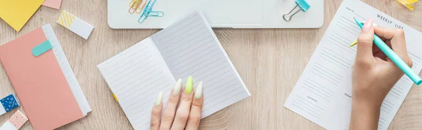 Cropped view of woman making notes in weekly list, sitting behind wooden table with notepad and stationery — Stock Photo