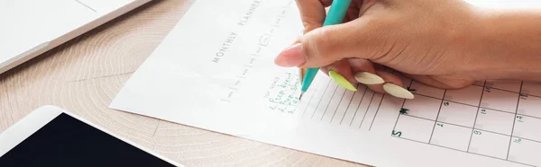 Vista recortada de la mujer sosteniendo pluma verde sobre planificador con notas - foto de stock