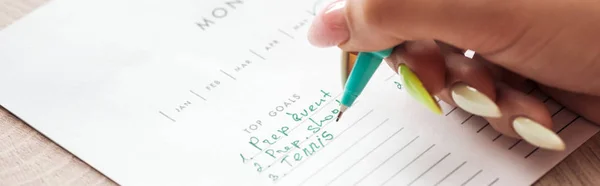 Cropped view of woman holding green pen over planner with notes — Stock Photo