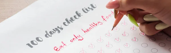 Cropped view of woman writing notes in 100 days check list, holding red pen in hand — Stock Photo
