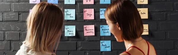 Two women standing near colorful sticker pads with notes on black brick wall — Stock Photo