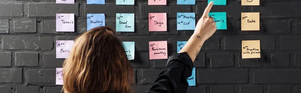 Vue arrière de la femme pointant du doigt les tampons autocollants colorés avec des notes sur le mur de briques noires — Photo de stock