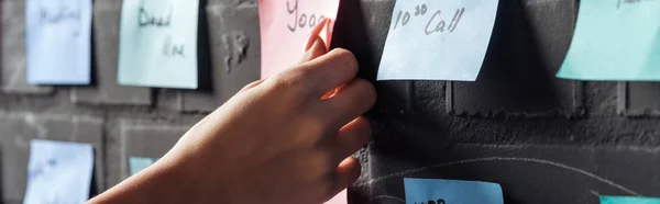 Vista recortada de la mujer adjuntar almohadillas adhesivas de colores con notas en la pared de ladrillo negro - foto de stock