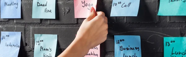 Vista recortada de la mujer adjuntar almohadillas adhesivas de colores con notas en la pared de ladrillo negro — Stock Photo