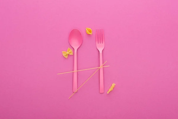 Rosa Plastiklöffel und -gabel und vier verschiedene Nudelsorten isoliert auf rosa — Stockfoto