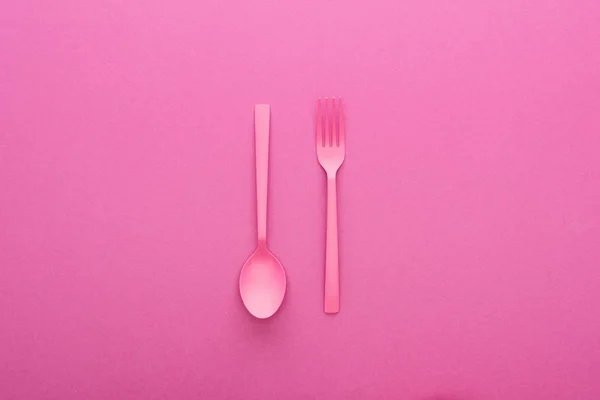 Pink plastic spoon upside down and fork on pink background — Stock Photo