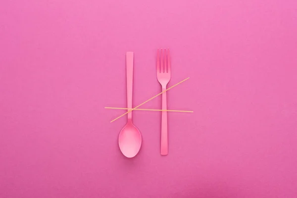 Colher de plástico rosa de cabeça para baixo e garfo com espaguete isolado em rosa — Fotografia de Stock