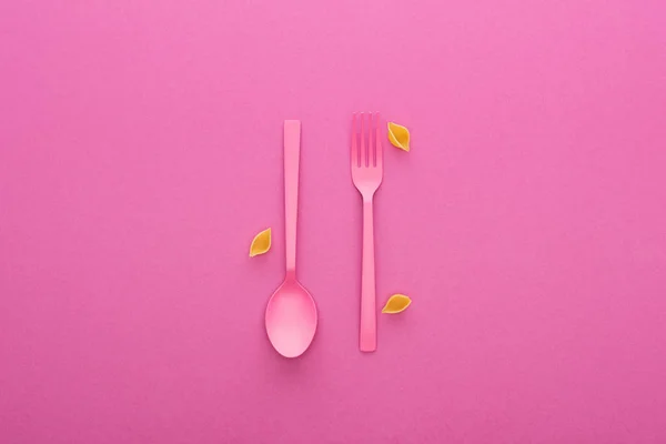 Tenedor de plástico rosa y cuchara al revés y conchas crudas macarrones aislados en rosa - foto de stock