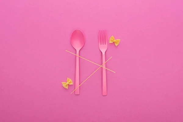 Cucchiaio e forchetta di plastica rosa, spaghetti e due farfalle crude isolate su rosa — Foto stock