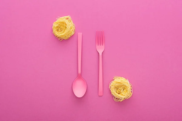 Pink plastic fork and spoon upside down near vermicelli pasta on pink background — Stock Photo
